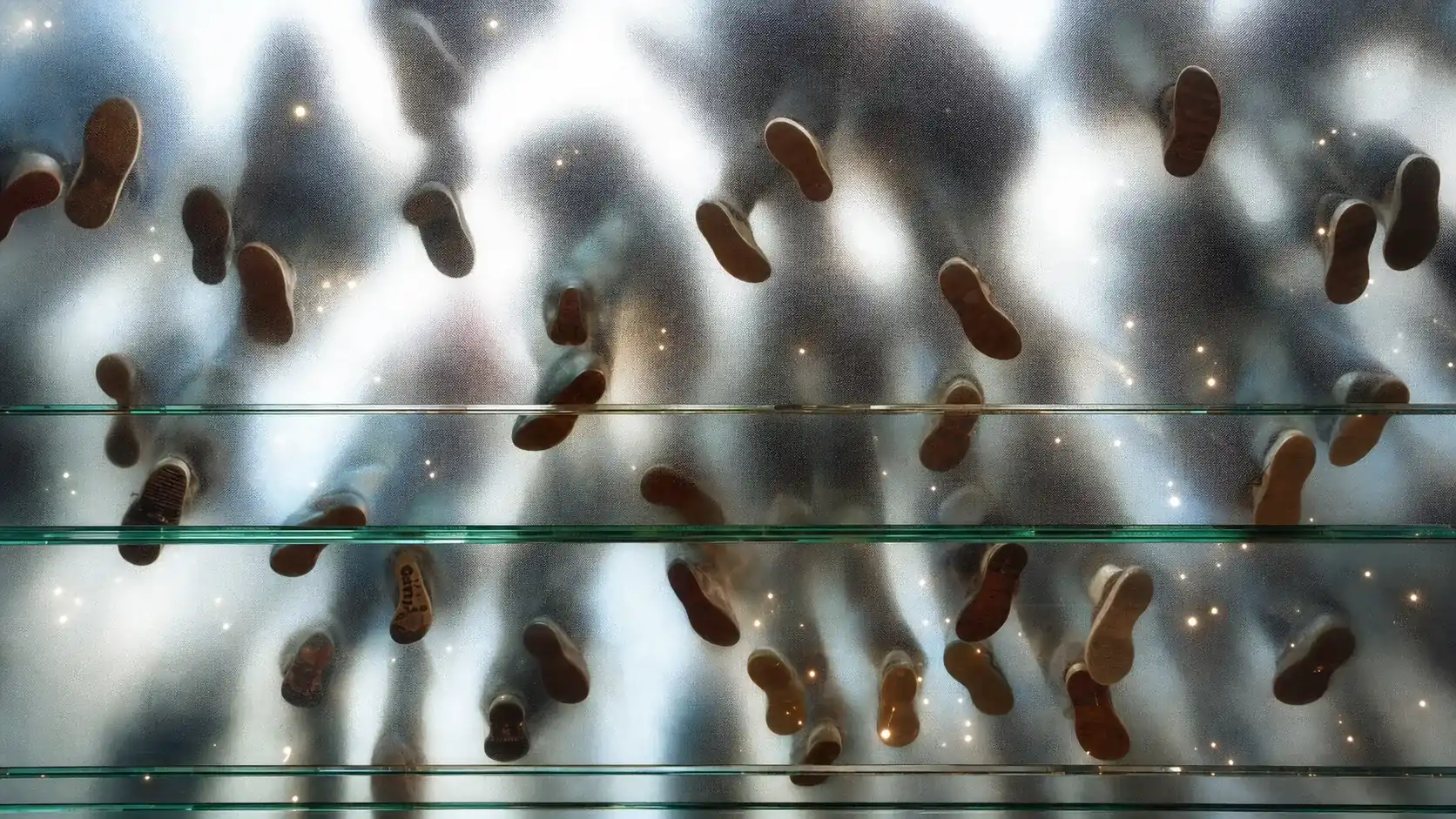 Blick von unten durch einen gläsernen Boden auf die Schuhsohlen vieler Menschen
